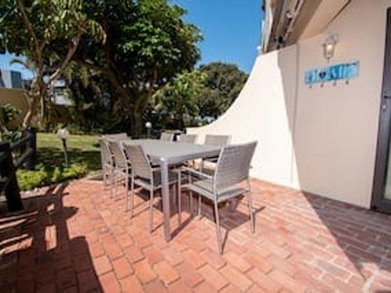 A private outdoor patio area featuring red brick paving, an exterior wall light, and direct access to the apartment through a sliding glass door.