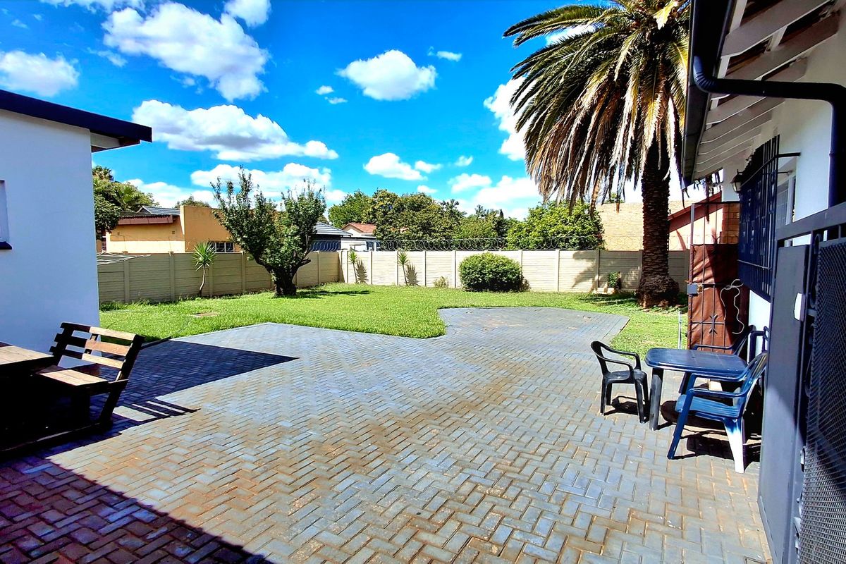 A spacious rear garden featuring a paved patio area, well-maintained lawn, and secure perimeter walling.