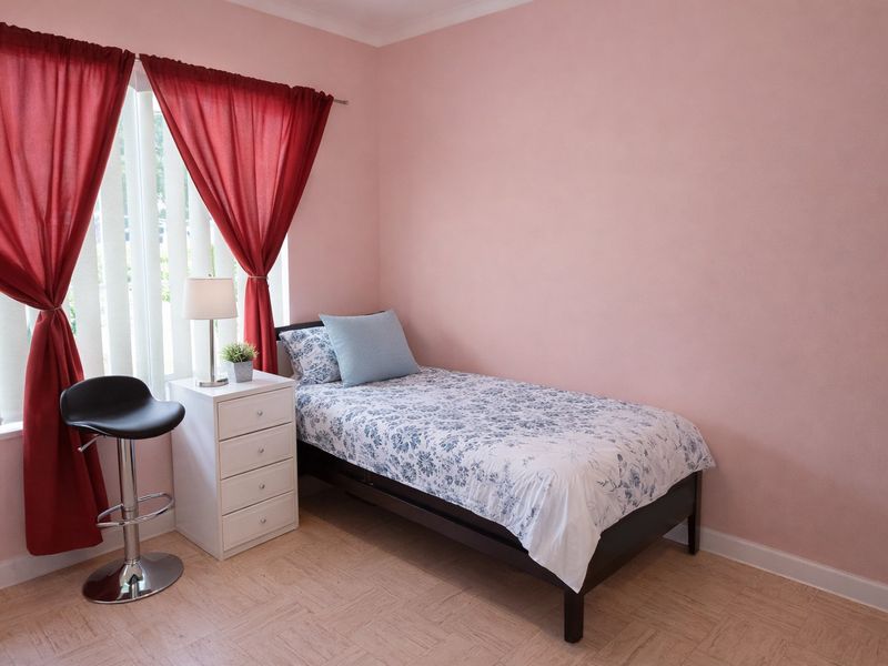 A bedroom featuring parquet flooring and vertical blinds, providing a functional space with neutral wall finishes.