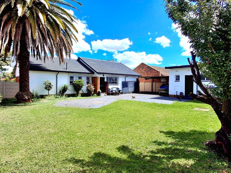 A view of the rear exterior of the house featuring a paved driveway, a well-maintained lawn, and a secure boundary wall.