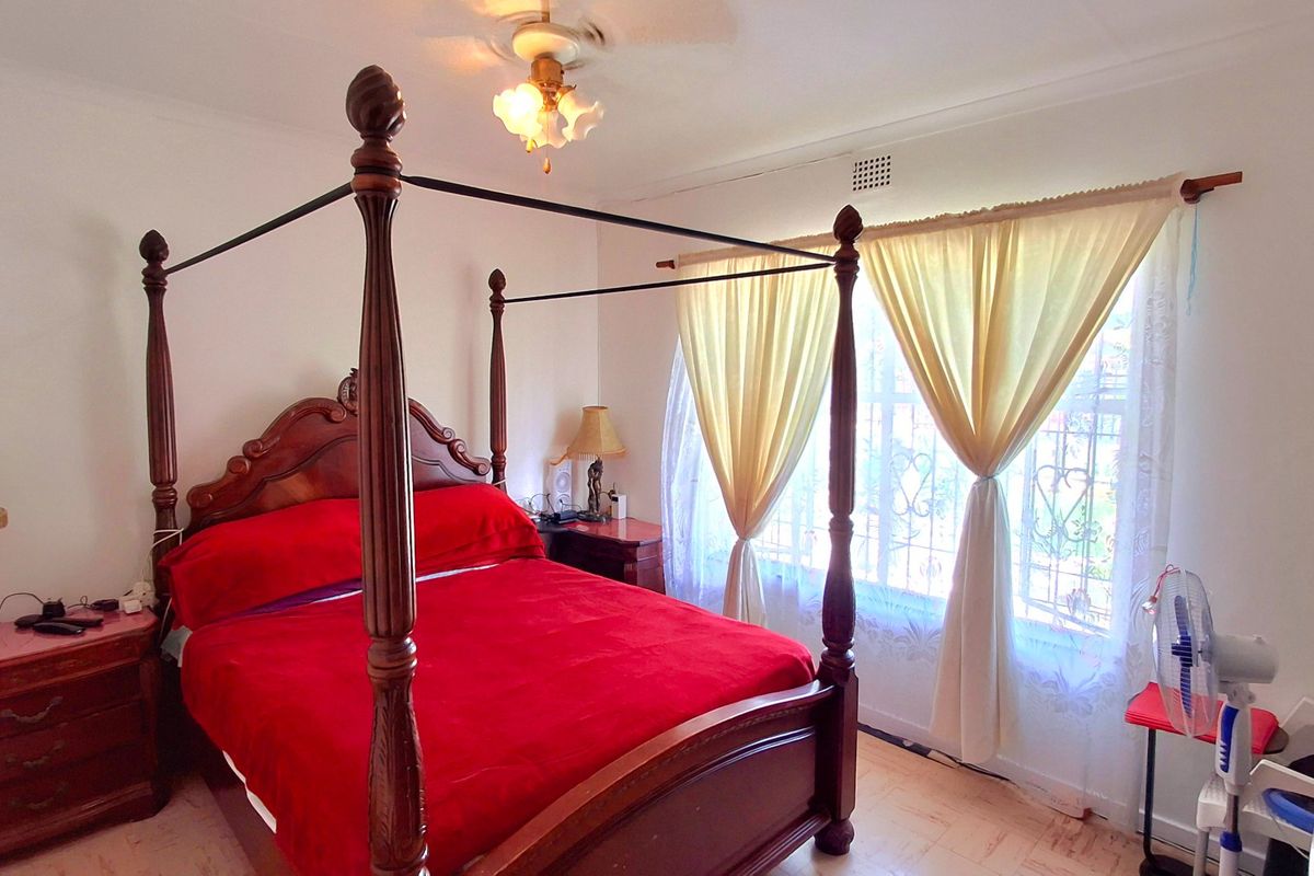 A bedroom featuring laminate flooring, a ceiling fan, and security bars on the window.