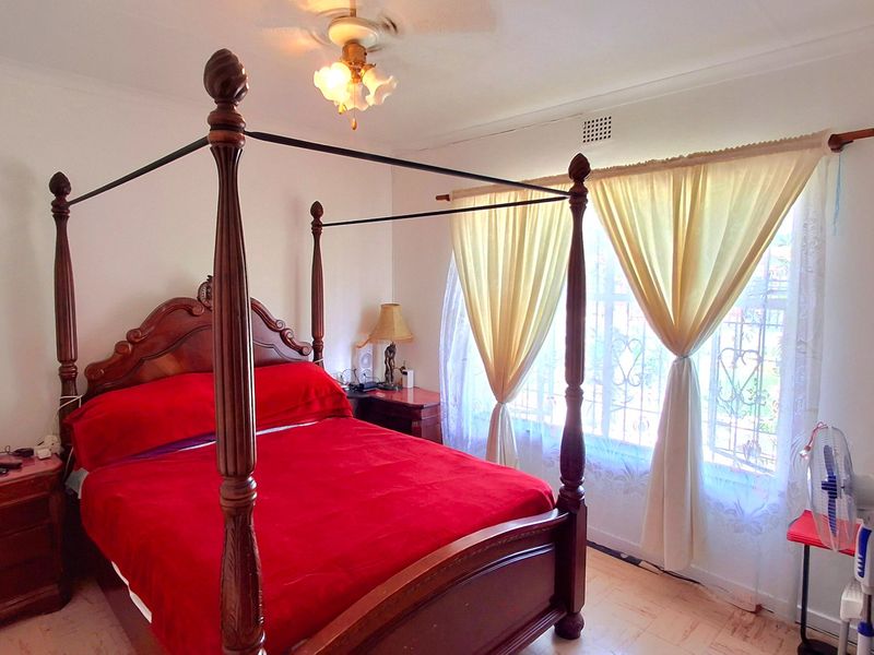 A bedroom featuring laminate flooring, a ceiling fan, and security bars on the window.
