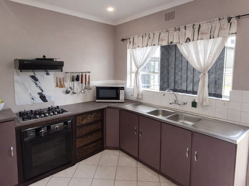 A functional kitchen featuring built-in cabinetry, a gas hob with extractor, integrated oven, and a double bowl stainless steel sink with tiled splashback.
