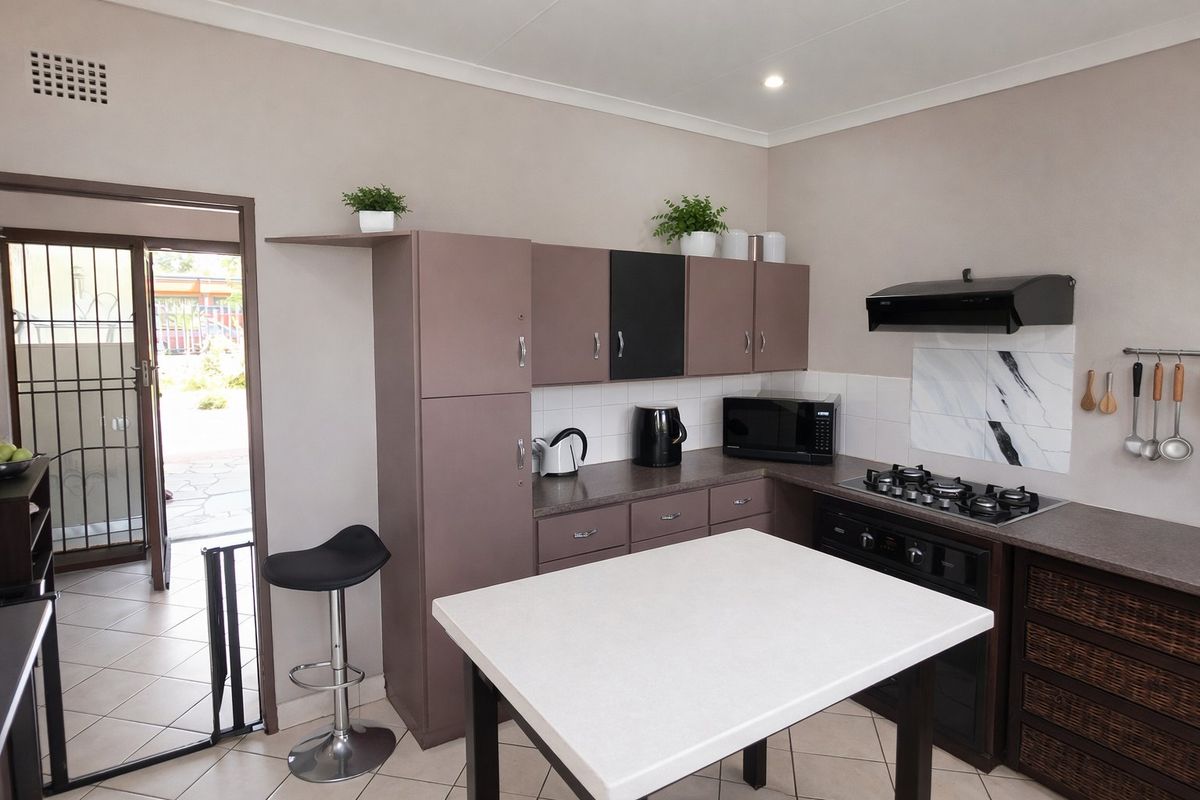 A functional kitchen featuring built-in cabinetry, a gas hob with extractor fan, and direct access to an outdoor area through a security gate.
