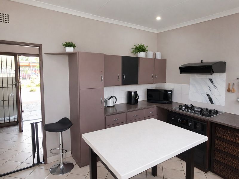 A functional kitchen featuring built-in cabinetry, a gas hob with extractor fan, and direct access to an outdoor area through a security gate.