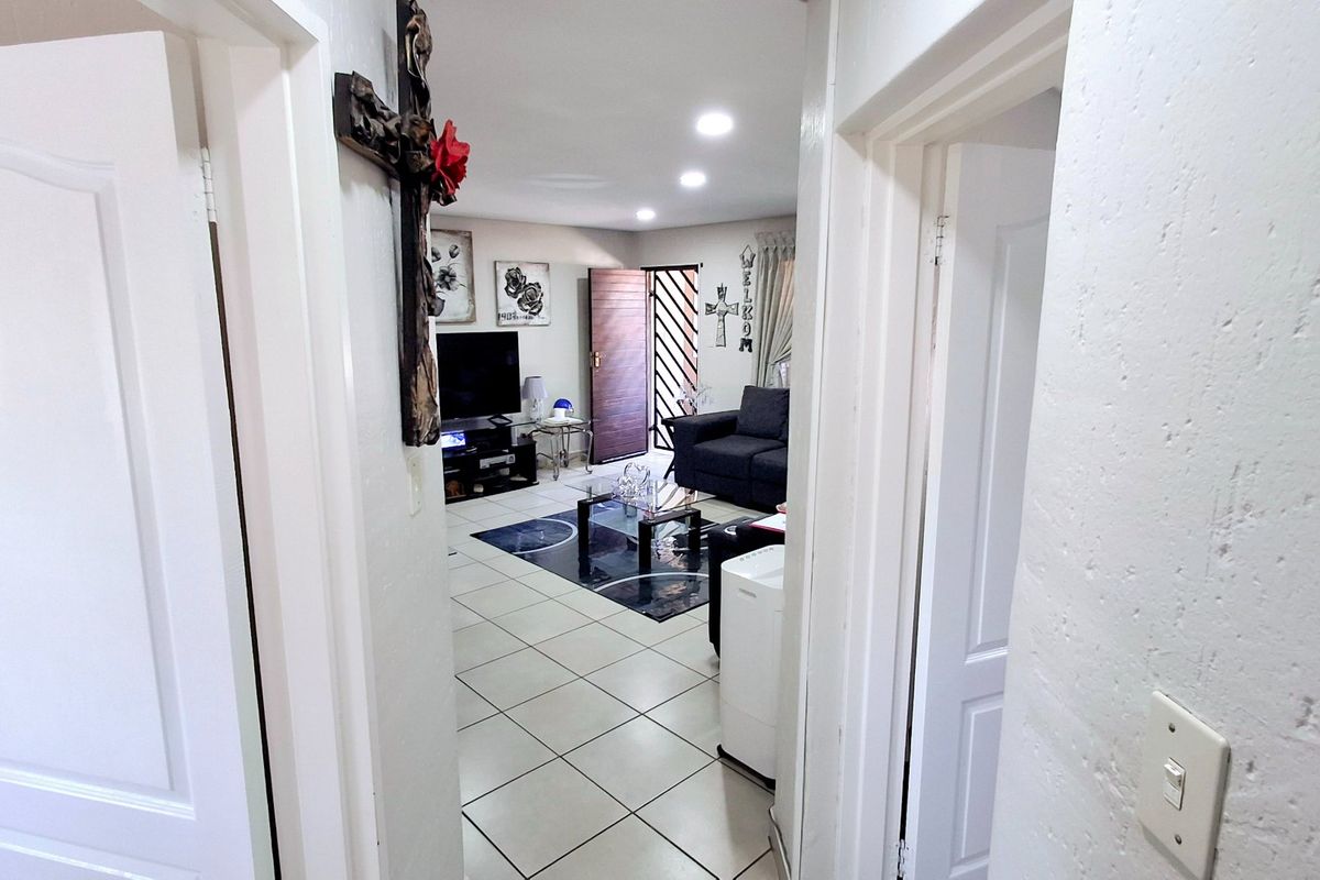 A view from the hallway into the living area, featuring tiled flooring, recessed lighting, and a secure entrance door.
