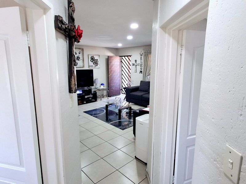 A view from the hallway into the living area, featuring tiled flooring, recessed lighting, and a secure entrance door.