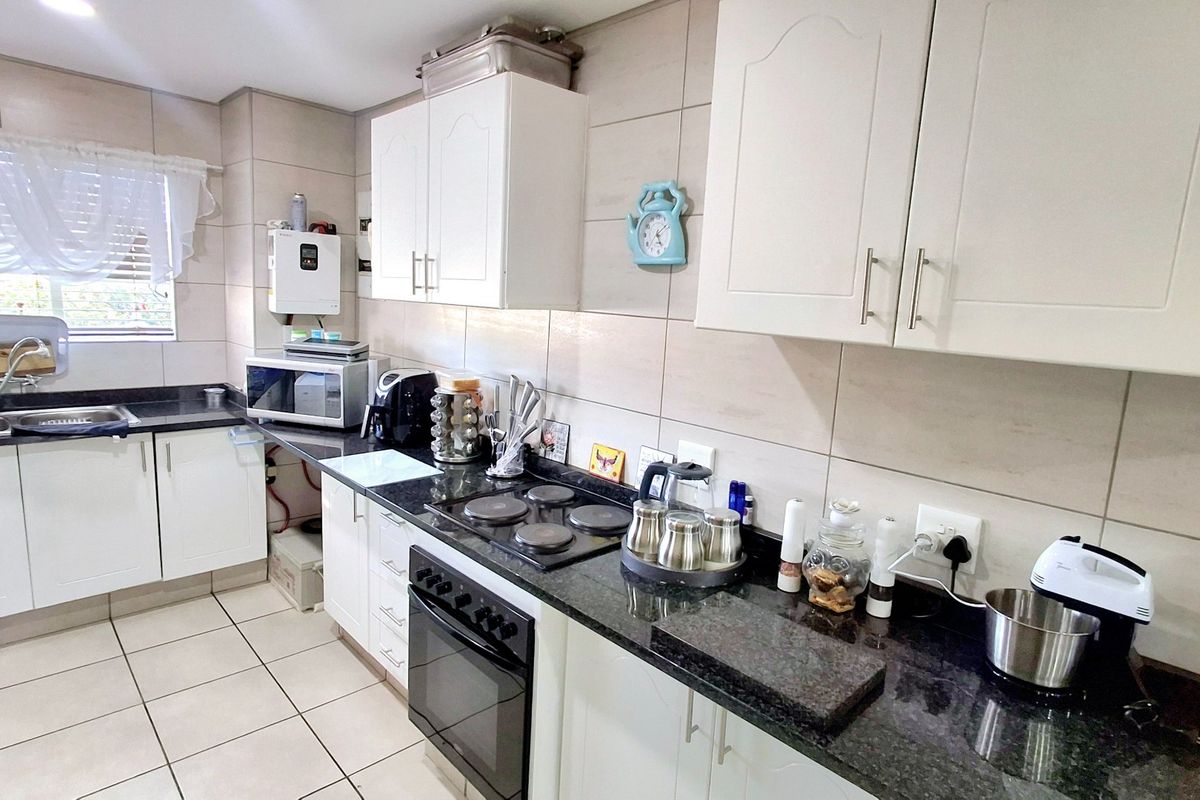 Functional kitchen featuring white cabinetry, dark granite countertops, integrated electric hob and oven, tiled backsplash, and tiled flooring.