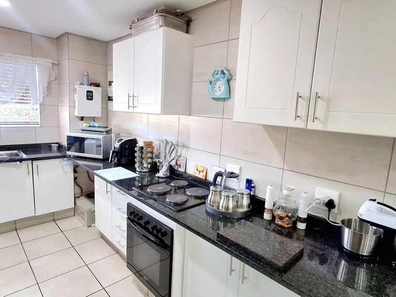 Functional kitchen featuring white cabinetry, dark granite countertops, integrated electric hob and oven, tiled backsplash, and tiled flooring.