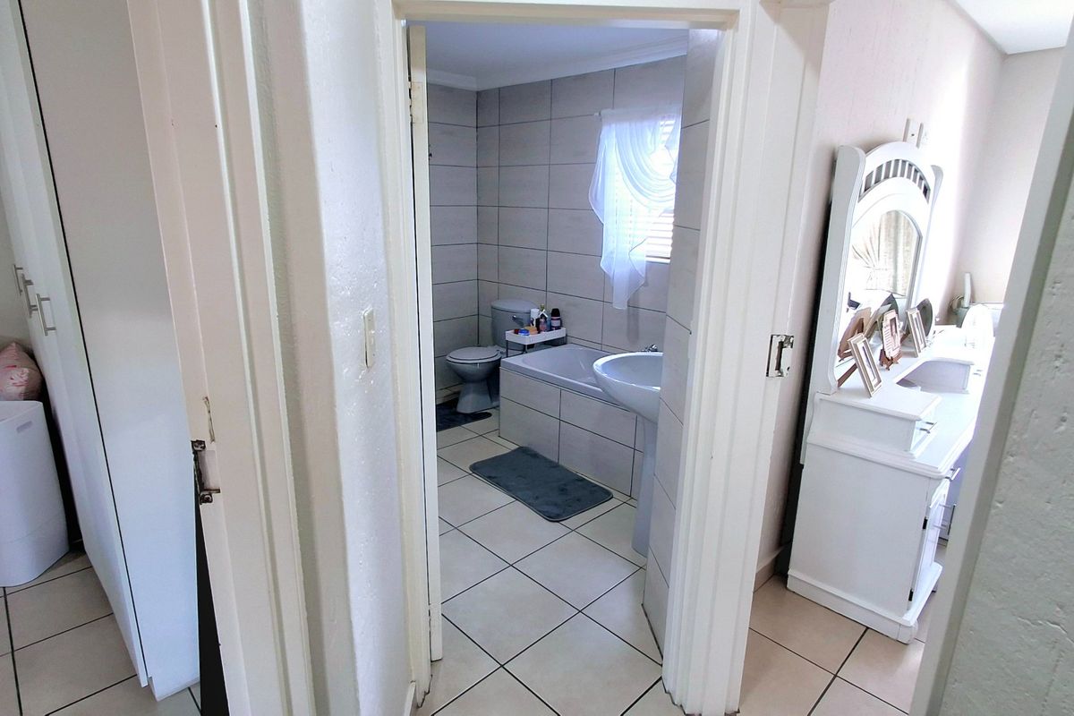 A functional bathroom featuring tiled walls and flooring, equipped with a bathtub, pedestal basin, and toilet, accessible from the adjacent bedroom area.