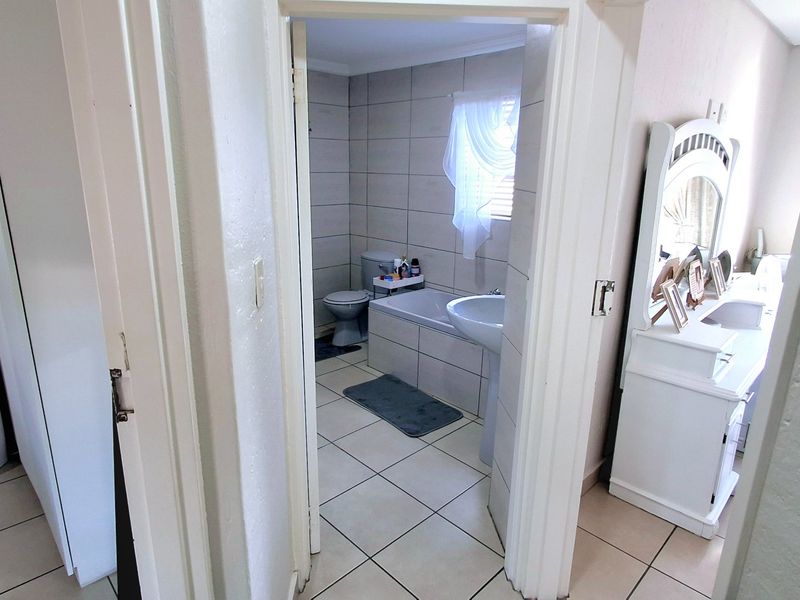 A functional bathroom featuring tiled walls and flooring, equipped with a bathtub, pedestal basin, and toilet, accessible from the adjacent bedroom area.