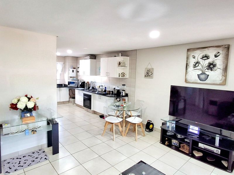 Open-plan living and kitchen area featuring tiled flooring, modern white cabinetry, and integrated cooking appliances in a bright, functional layout.