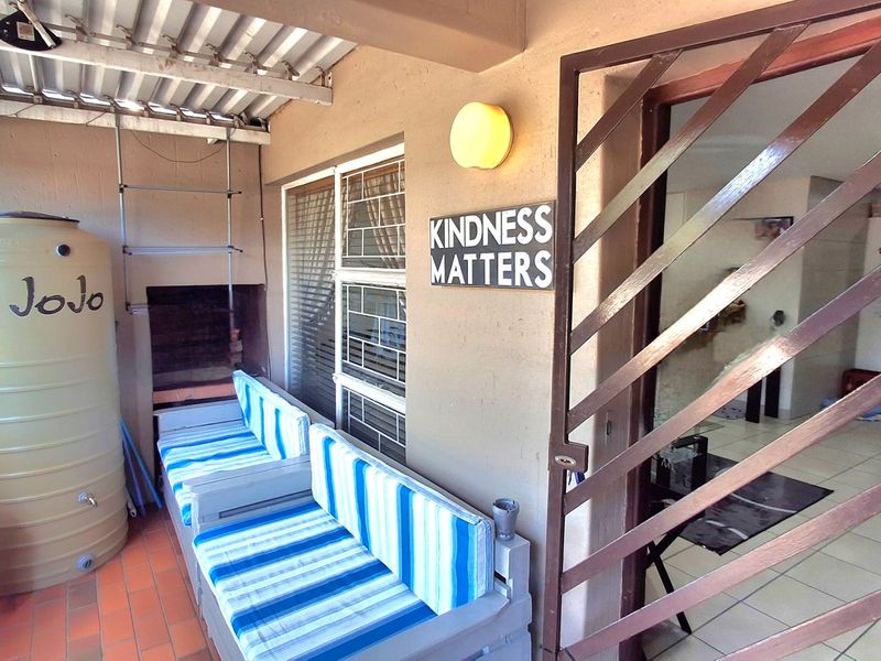 Covered patio area featuring a built-in braai, water storage tank, and secure metal gate access to the apartment interior.