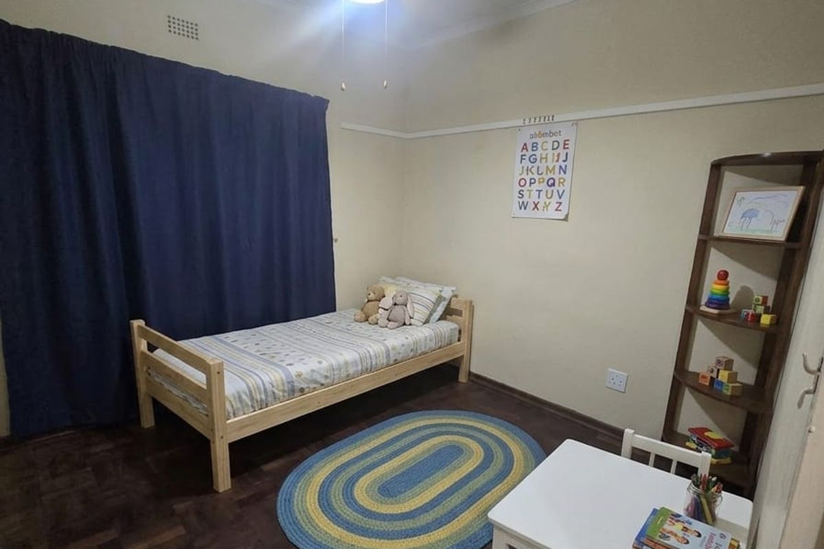 A well-proportioned bedroom featuring classic parquet flooring, a ceiling fan, and a traditional picture rail, offering a clean and functional living space.