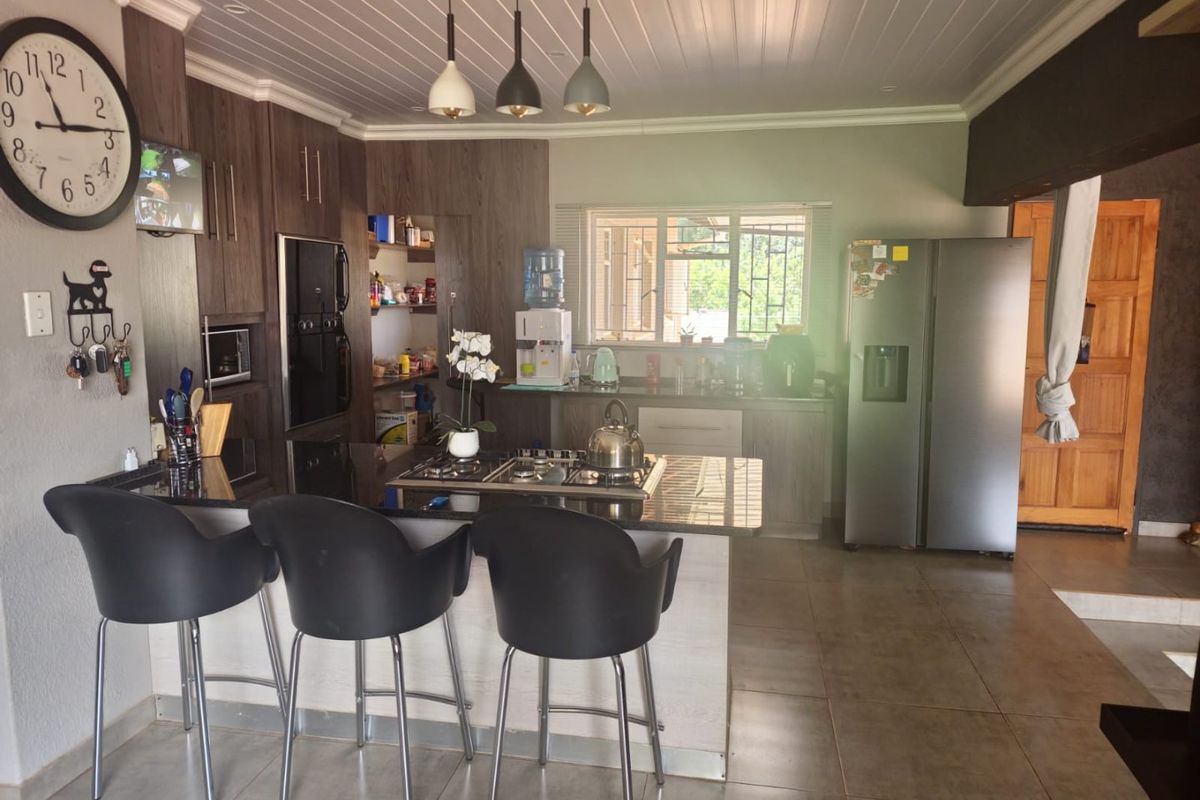 A functional kitchen featuring dark wood cabinetry, granite countertops, a central gas hob, and integrated appliances with tiled flooring and modern pendant lighting.