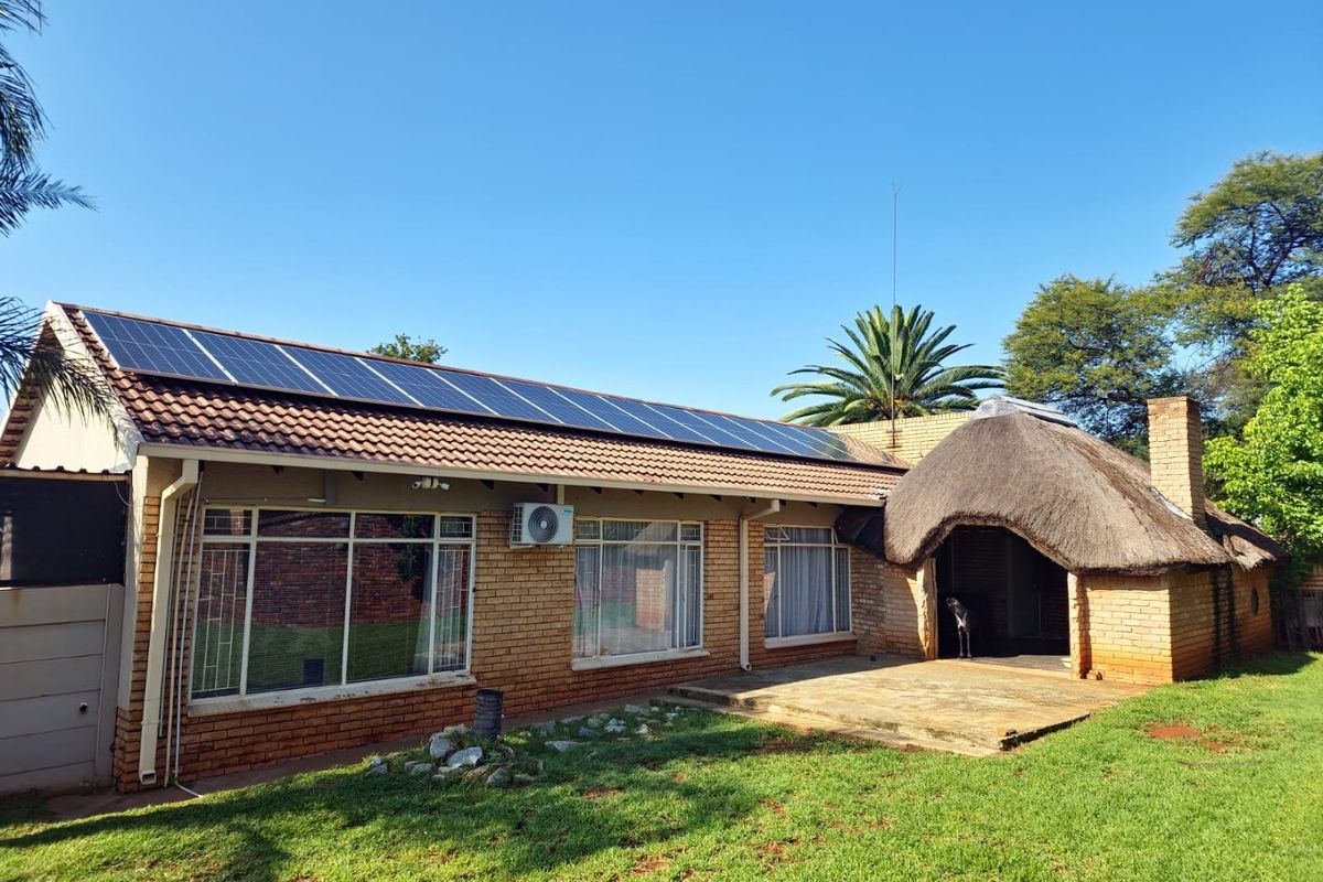 Rear view of the house featuring a brick facade, tiled roof with integrated solar panels, a thatched roof section, and a concrete patio area.