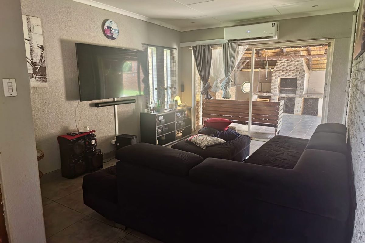 A comfortable living room featuring tiled flooring, a wall-mounted air conditioning unit, and large sliding glass doors providing direct access to an outdoor patio area.