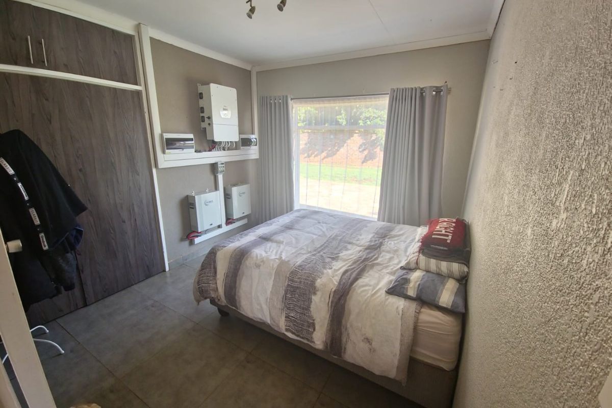 Bedroom featuring built-in cupboards, tiled flooring, and a wall-mounted solar inverter and battery system.