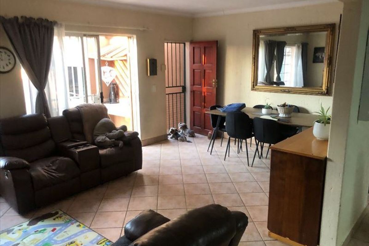 Open plan living and dining area featuring tiled flooring, sliding glass doors to the patio, and a security gate at the entrance.