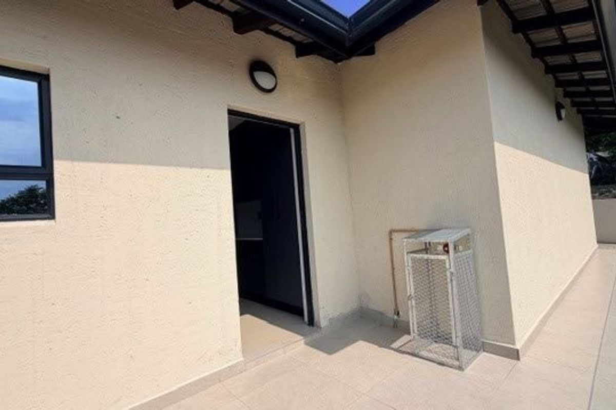 A view of the exterior rear patio area featuring tiled flooring, a wall-mounted light fixture, and a secure gas bottle cage.
