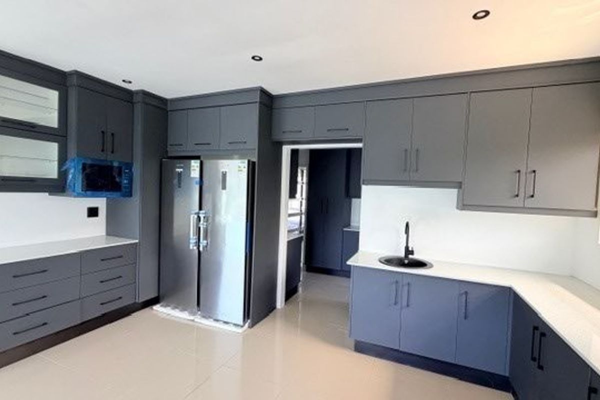 Modern kitchen featuring dark grey cabinetry, white stone countertops, integrated storage, and a sleek black sink fixture.