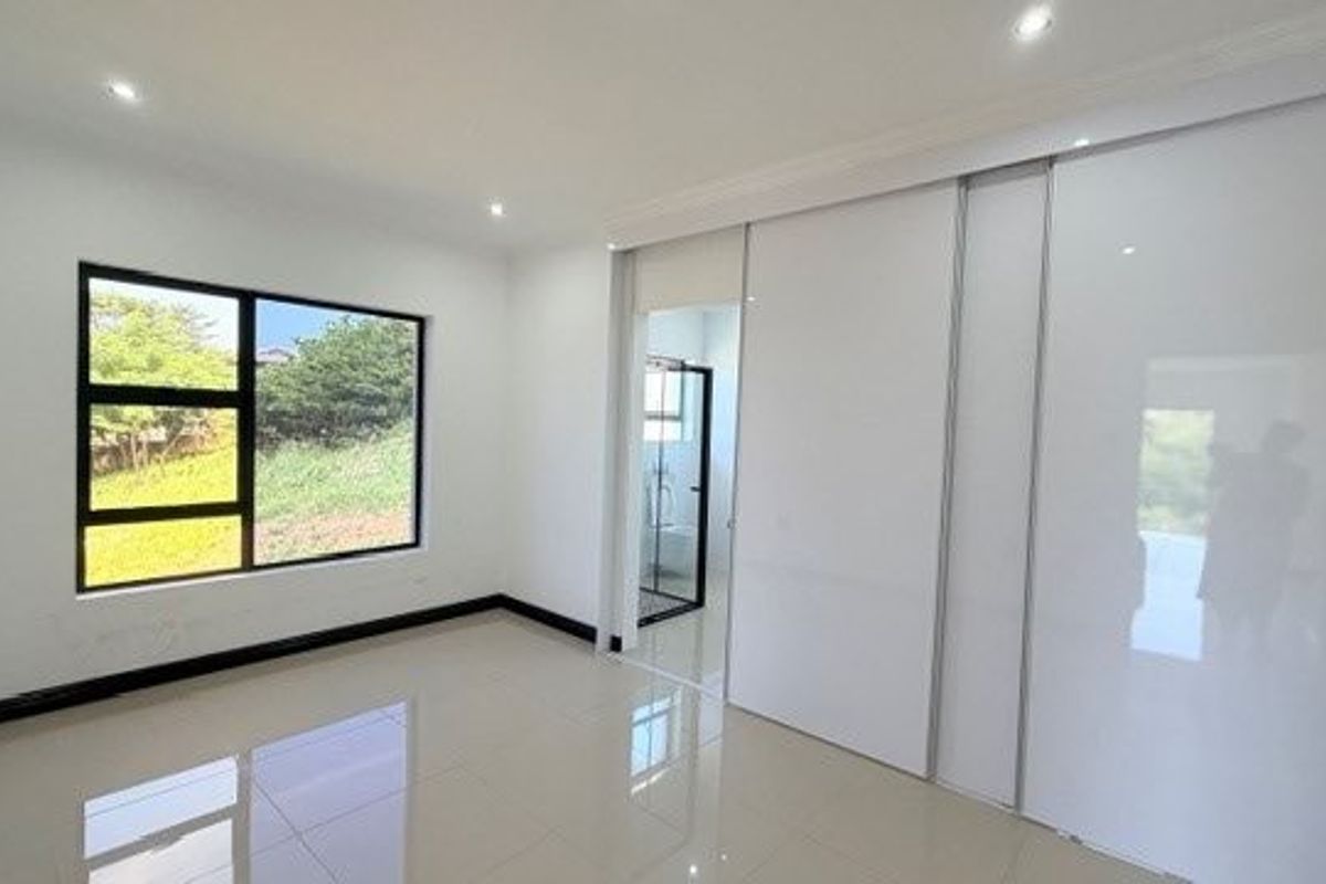 A bright, modern bedroom featuring large windows, polished tile flooring, recessed ceiling lighting, and sleek built-in sliding door wardrobes with an en-suite bathroom.