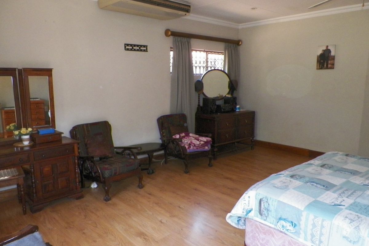 Spacious bedroom featuring laminate flooring, a ceiling fan, and a wall-mounted air conditioning unit, with security bars installed on the window.