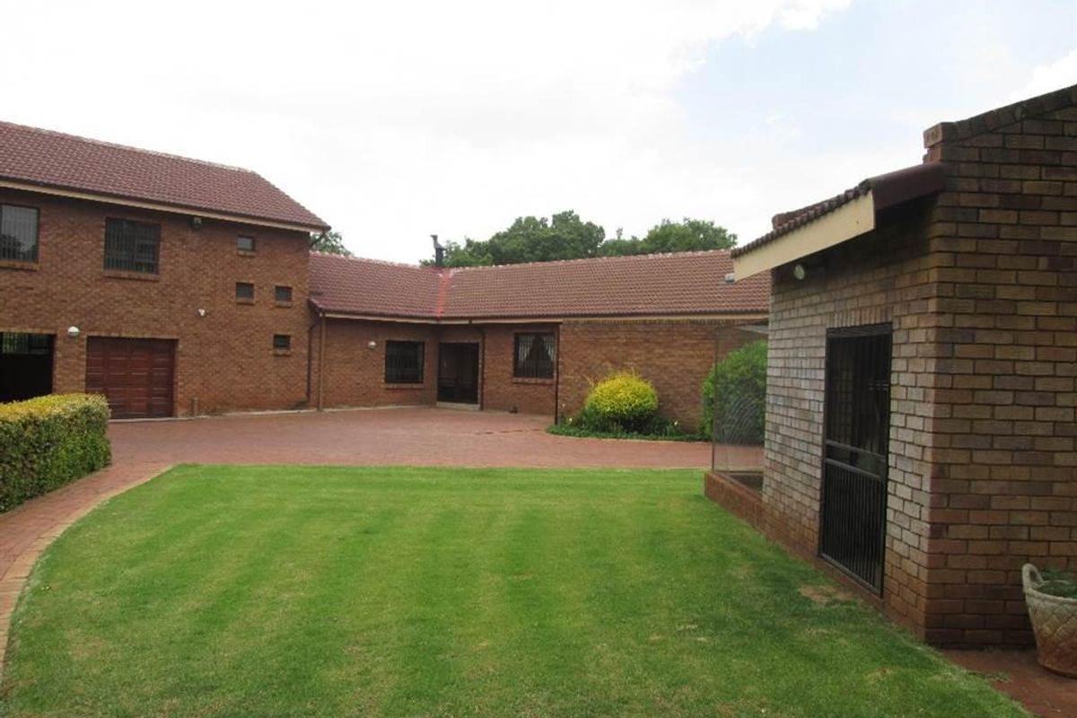 A view of the rear exterior featuring a brick house facade, paved driveway, and a well-maintained lawn area.