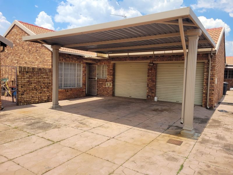 A double garage with a covered carport, featuring brick construction, tiled roofing, and a paved driveway area.