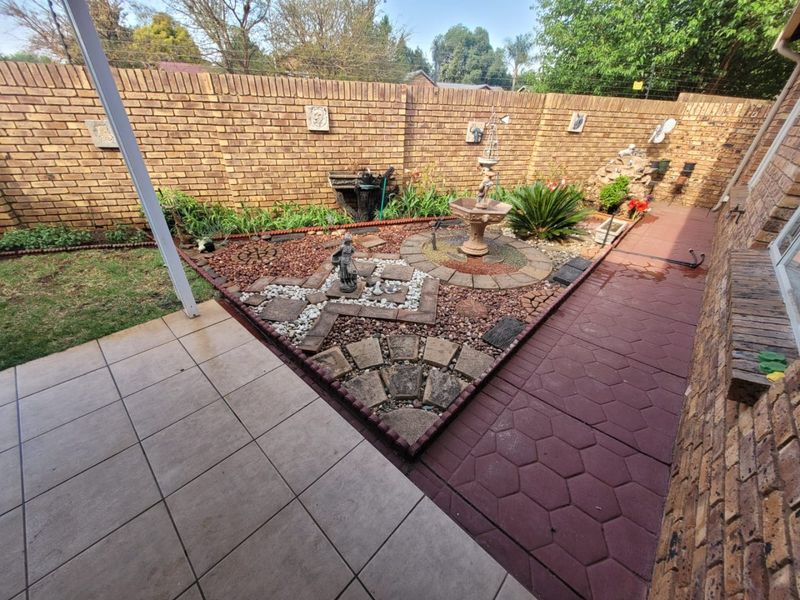 A private rear garden featuring a brick boundary wall, paved patio area, and landscaped stone pathways with a central water feature.