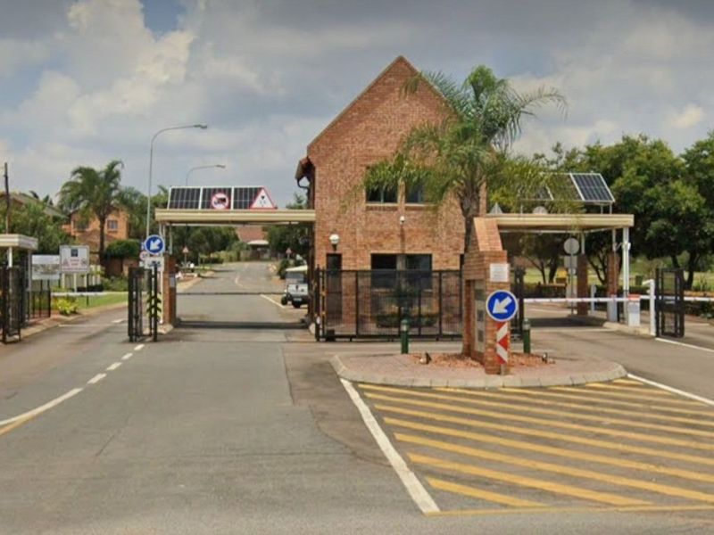 The entrance to the townhouse complex features a brick security gatehouse, automated boom gates, and solar-powered infrastructure for controlled access.