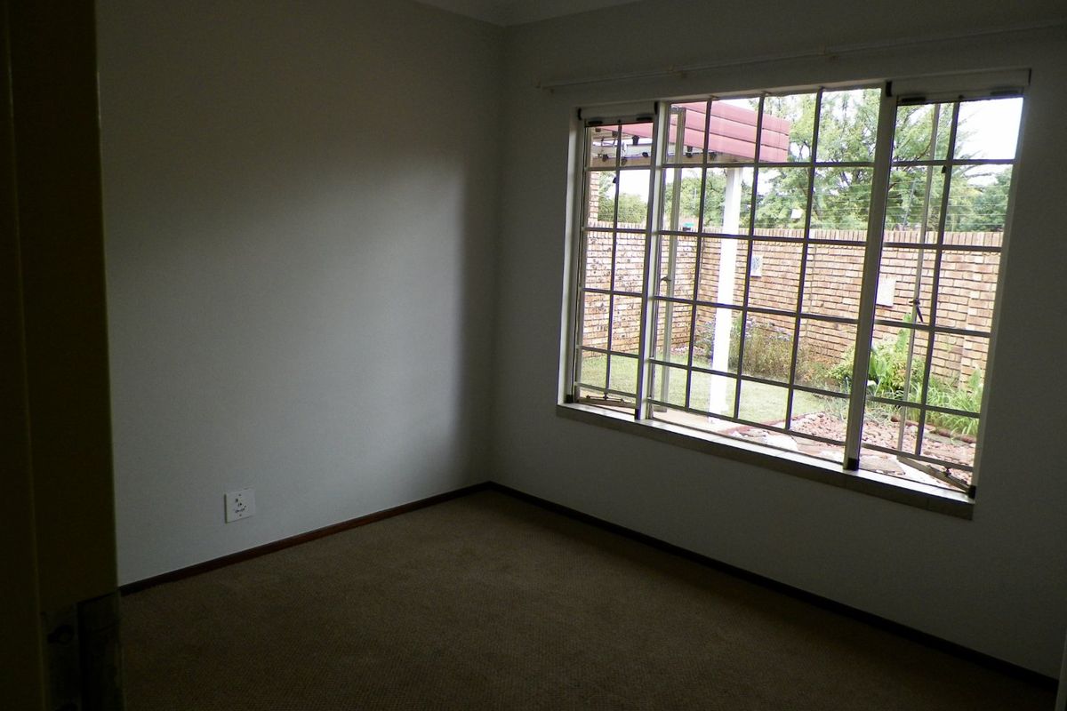 An empty bedroom featuring carpeted flooring, a large window with security bars, and neutral wall finishes, offering a blank canvas for personalization.
