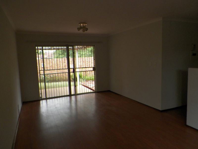 An empty living room featuring laminate flooring and a sliding glass door with security gate, providing direct access to the rear patio area.