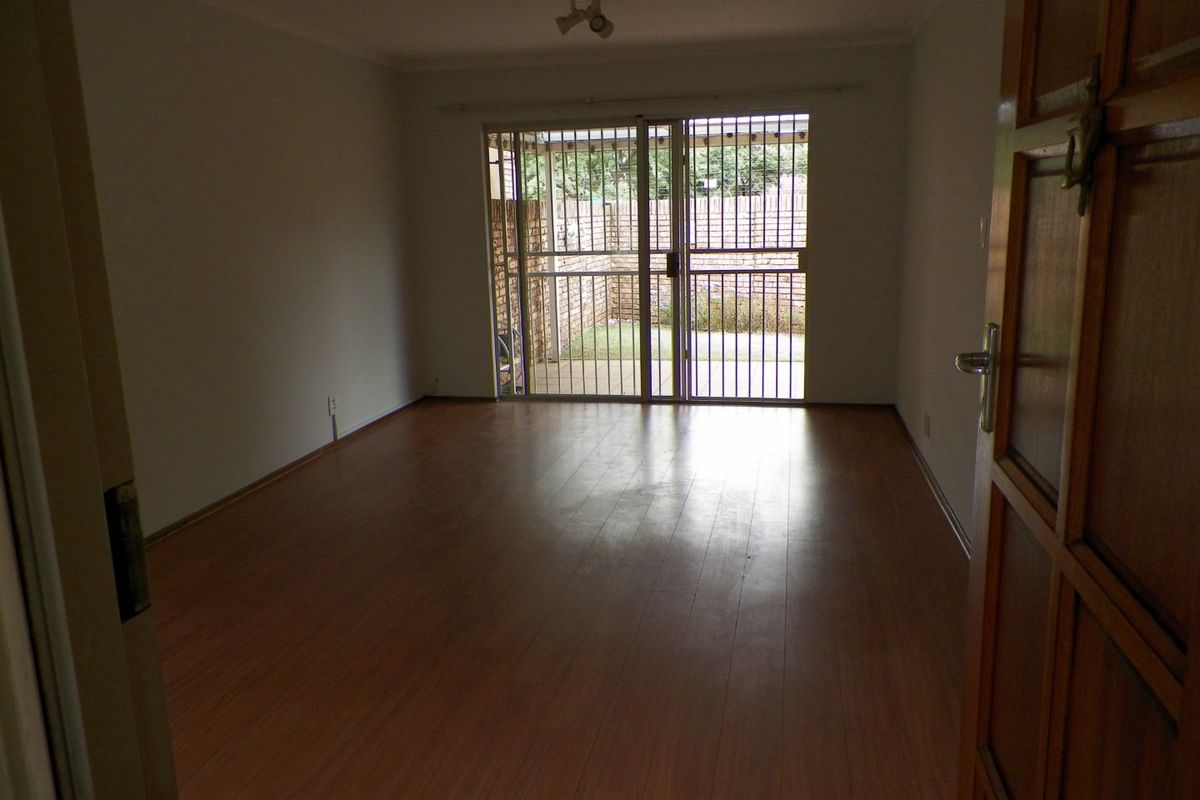 An empty living room featuring laminate flooring and a sliding security gate providing access to the rear patio area.