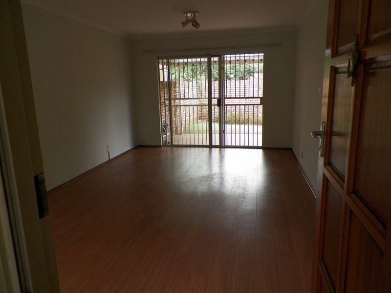 An empty living room featuring laminate flooring and a sliding security gate providing access to the rear patio area.