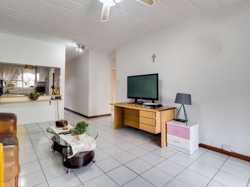 Open plan living area featuring tiled flooring, a ceiling fan, and a convenient pass-through window connecting to the kitchen space.
