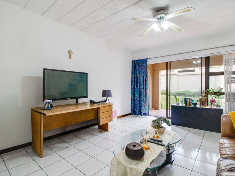 A living room featuring white tiled flooring, a ceiling fan, and a large sliding glass door providing access to an outdoor patio area.