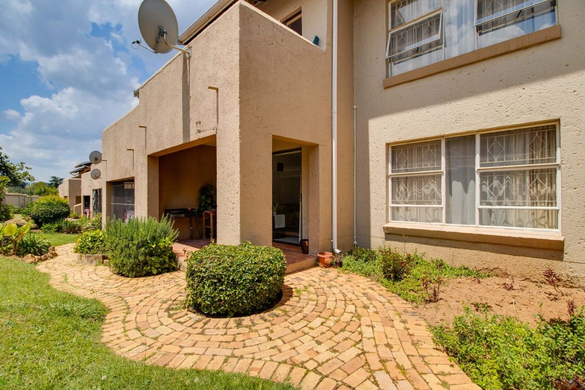 Rear view of the apartment featuring a covered patio, brick paved garden path, and established landscaping.