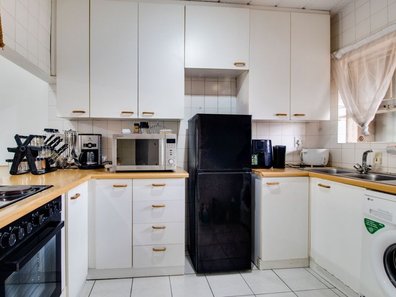 A functional kitchen featuring white cabinetry, laminate countertops, built-in oven, hob, and tiled finishes, offering a practical layout for daily meal preparation.