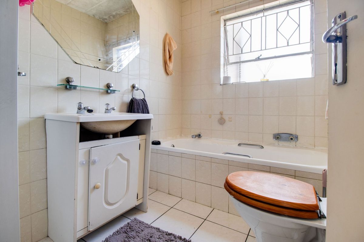 A dated bathroom featuring a built-in vanity, bathtub, and toilet with tiled finishes, offering potential for modernization and renovation.