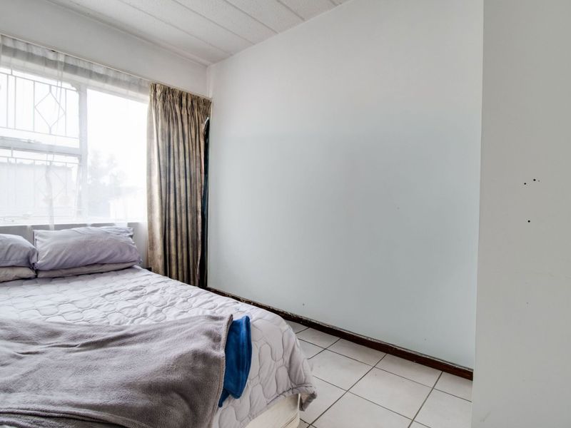 A bedroom featuring tiled flooring and a window with security bars, requiring cosmetic updates to the walls and skirting boards.