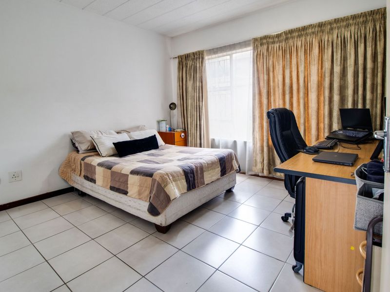 A functional bedroom featuring tiled flooring and large windows with curtain tracks, providing a neutral space ready for personalization.