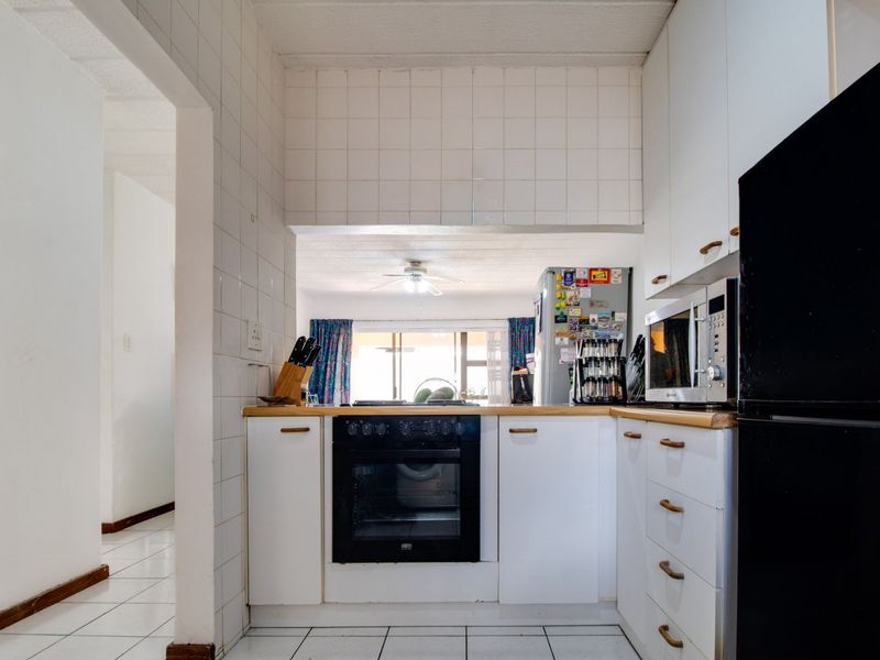A functional kitchen featuring white cabinetry, a built-in oven, and tiled finishes, with an open-plan layout connecting to the adjacent living area.