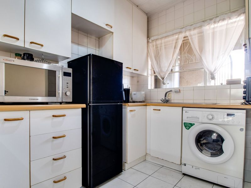 Compact kitchen featuring white cabinetry, laminate countertops, tiled backsplash, and integrated space for laundry appliances.
