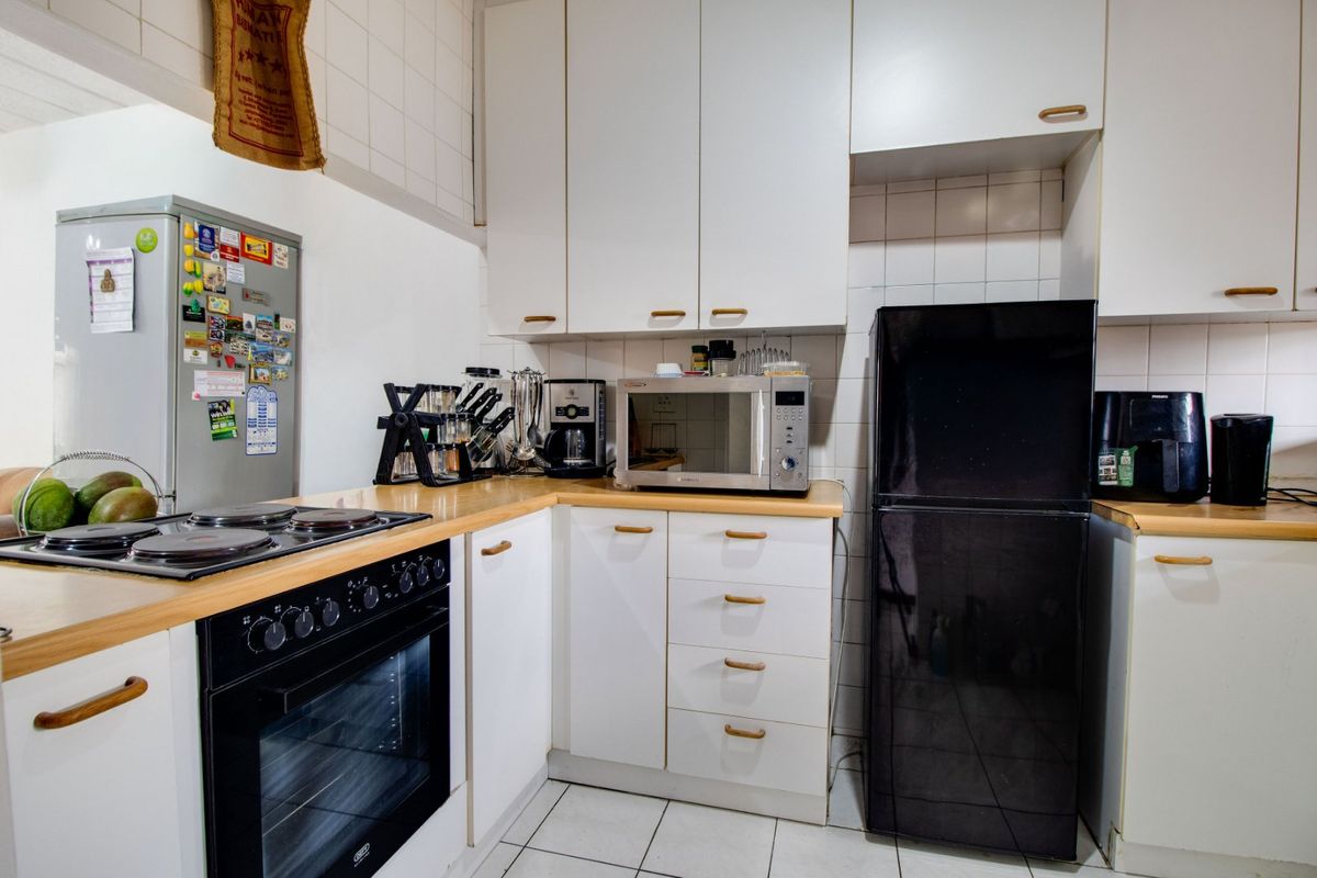 A functional kitchen featuring white cabinetry, laminate countertops, a built-in electric oven and hob, and tiled finishes throughout.