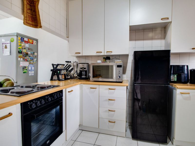 A functional kitchen featuring white cabinetry, laminate countertops, a built-in electric oven and hob, and tiled finishes throughout.