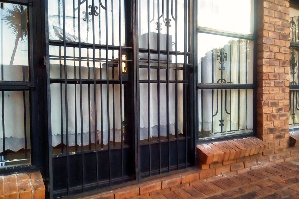 Exterior view of a brick facade featuring a black metal security gate and window frames, set against a paved brick patio area.