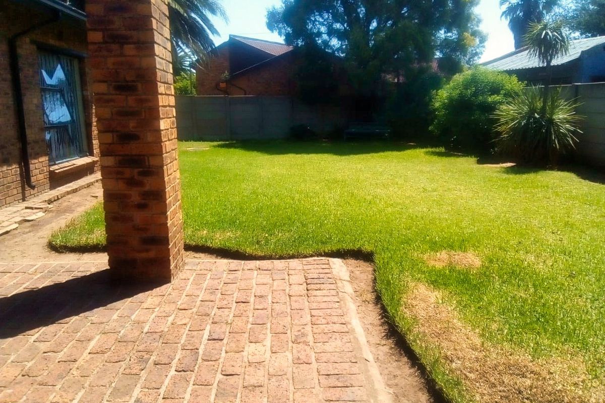 A private rear garden featuring a brick-paved patio area and a well-maintained lawn, enclosed by perimeter walling.