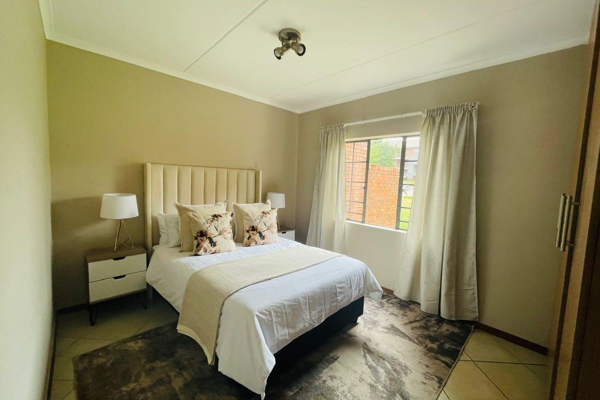A well-maintained bedroom featuring neutral wall tones, tiled flooring, and a window fitted with security bars.