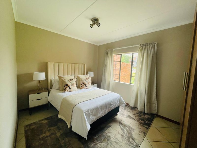 A well-maintained bedroom featuring neutral wall tones, tiled flooring, and a window fitted with security bars.